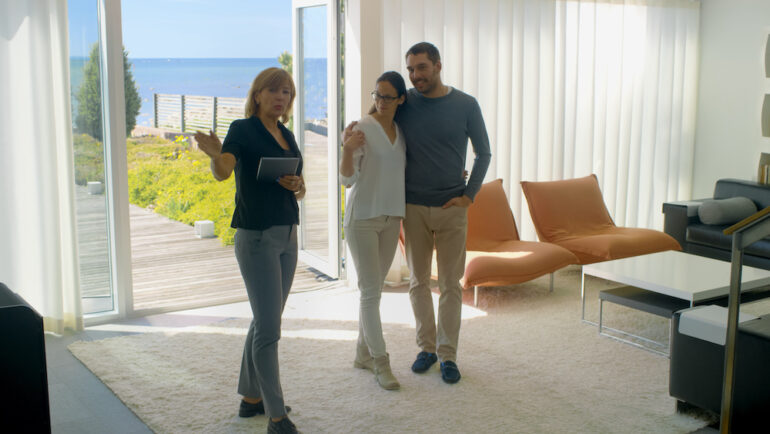 A professional real estate agent shows stylish modern houses to a young couple.