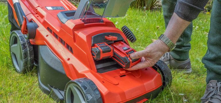 Male Gardener changing the battery on an electric, cordless lawn mower.