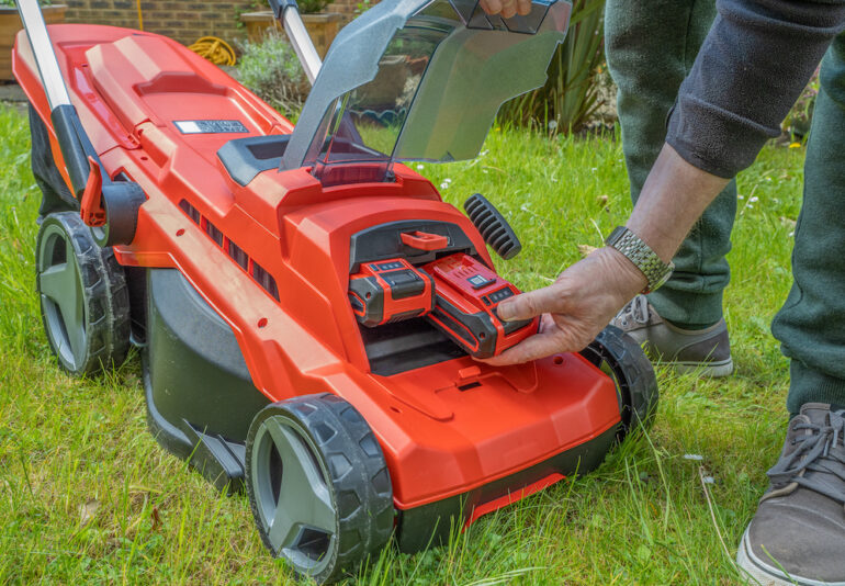 Male Gardener changing the battery on an electric, cordless lawn mower.