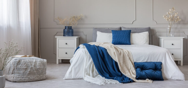Blue pillow and blanket on white bed sheets in a spacious bedroom interior.