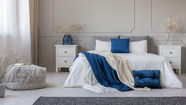 Blue pillow and blanket on white bed sheets in a spacious bedroom interior.