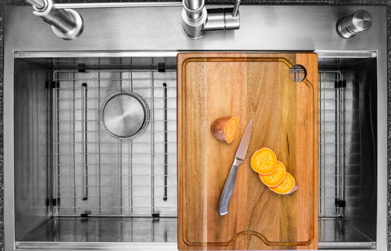 Workstation kitchen sink with cutting board used to slice a sweet potato