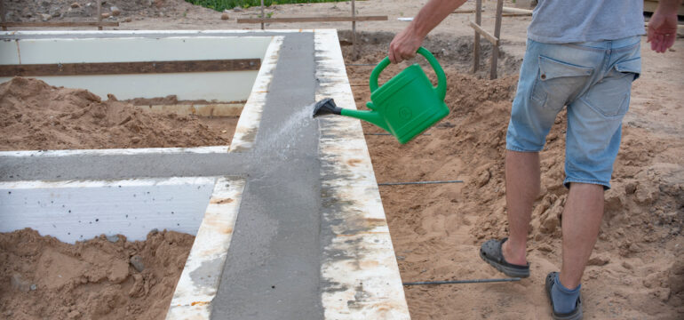 Concrete foundation for a new house. A man waters to prevent the foundation from cracking.