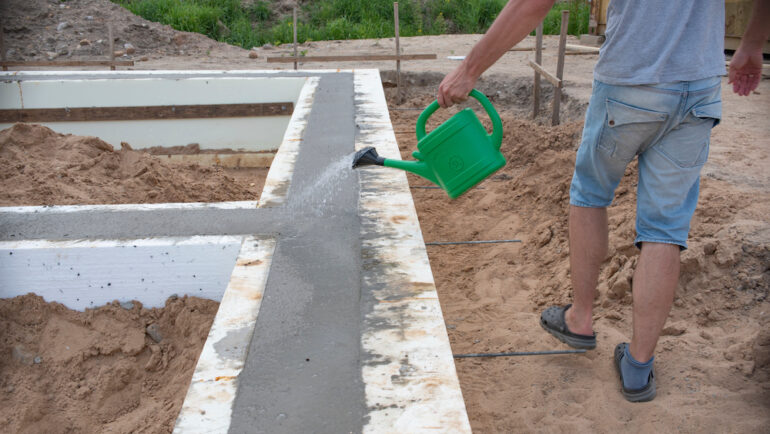Concrete foundation for a new house. A man waters to prevent the foundation from cracking.