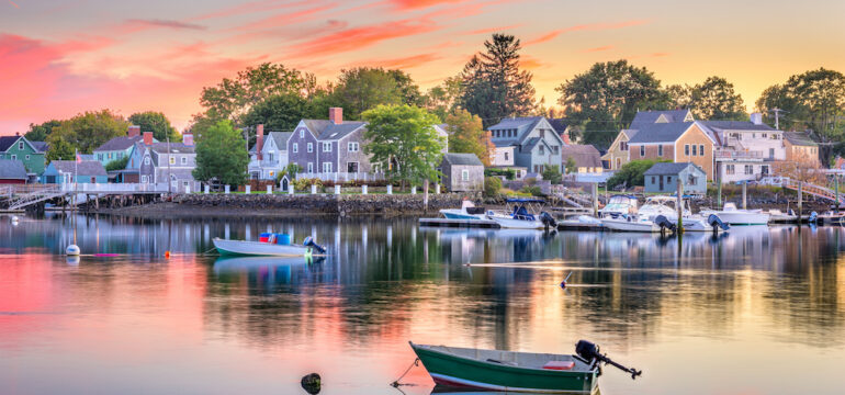 Waterfront property facing a bay with several boats in the harbor at sunset.