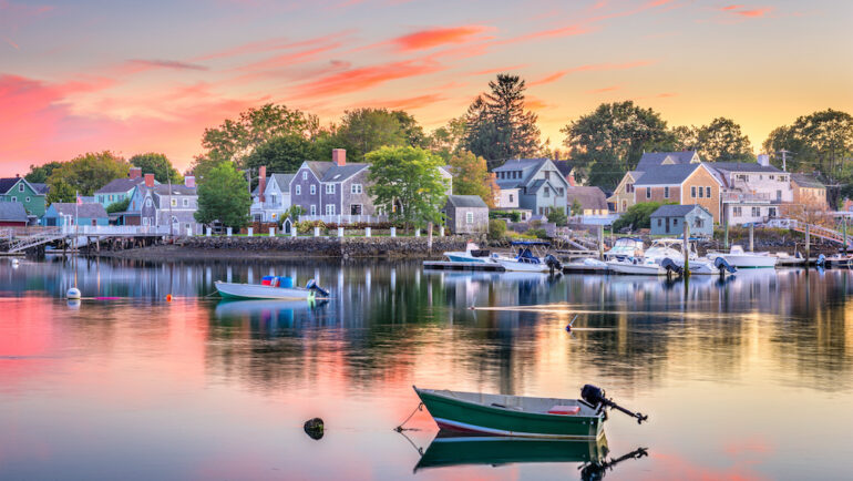 Waterfront property facing a bay with several boats in the harbor at sunset.