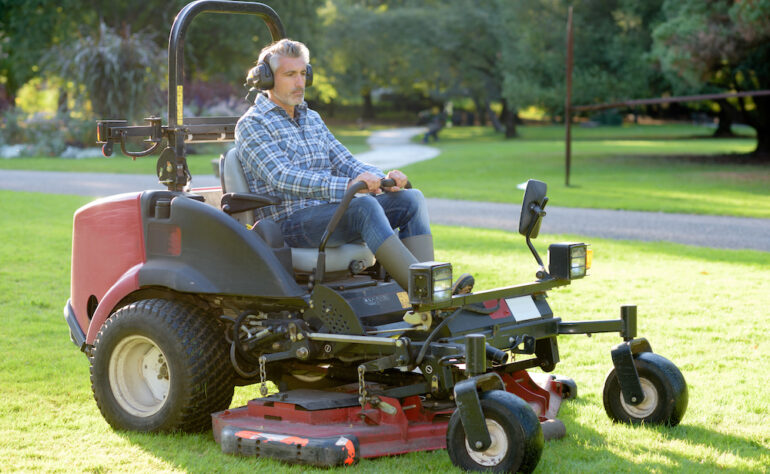 Ground maintenance man using a zero-turn lawnmower to cut the grass of a large property.