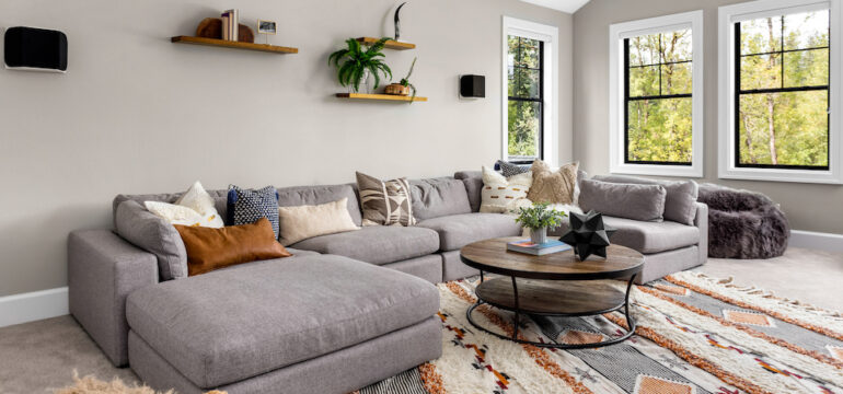 Grey L-shaped living sofa placed on colorful area rugs.