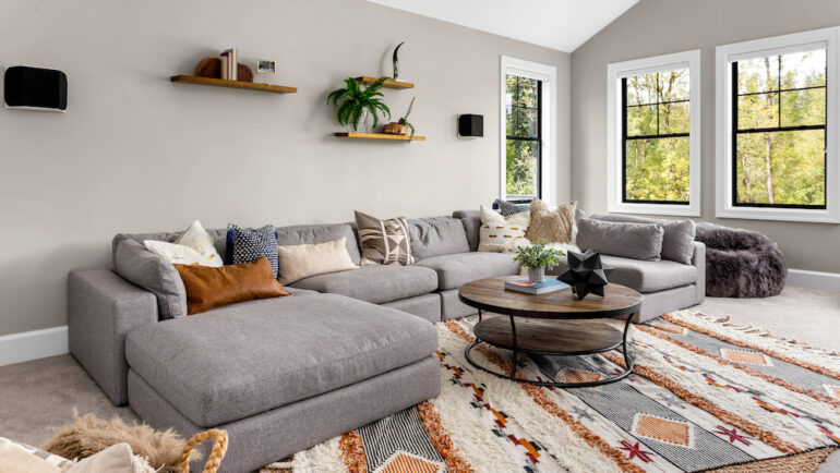 Grey L-shaped living sofa placed on colorful area rugs.