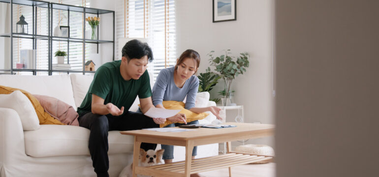 Young couple sitting on a white living room sofa calculating mortgage payments as interest rates increase.