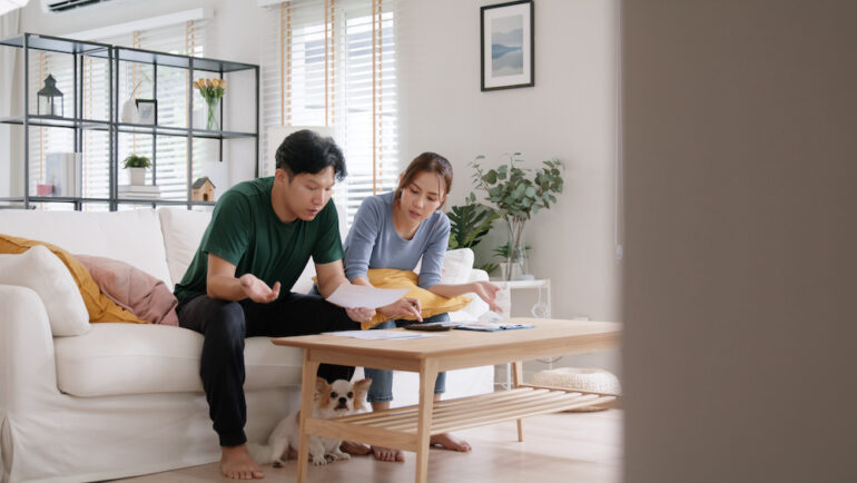 Young couple sitting on a white living room sofa calculating mortgage payments as interest rates increase.