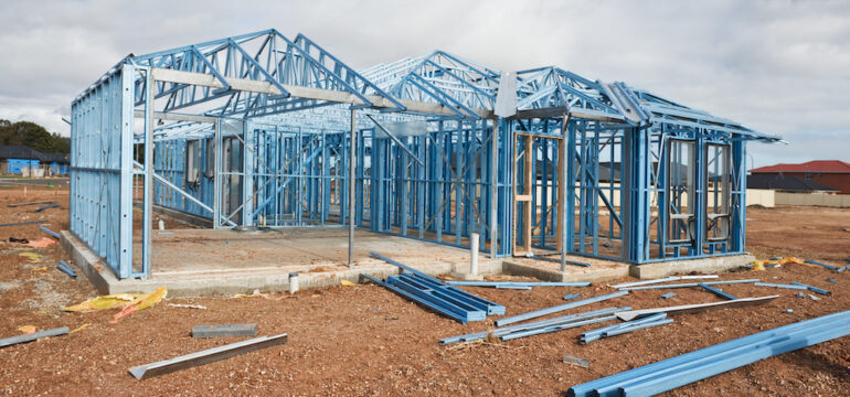 A new home is under construction using a steel frame against a cloudy sky.