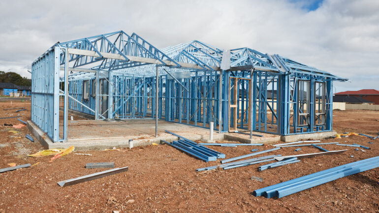 A new home is under construction using a steel frame against a cloudy sky.