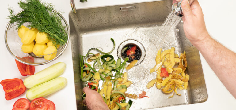 A man recycles food waste using a modern kitchen garbage disposal.