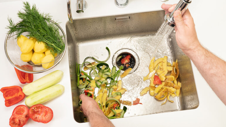 A man recycles food waste using a modern kitchen garbage disposal.