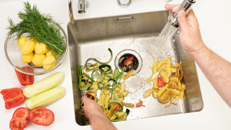 A man recycles food waste using a modern kitchen garbage disposal.