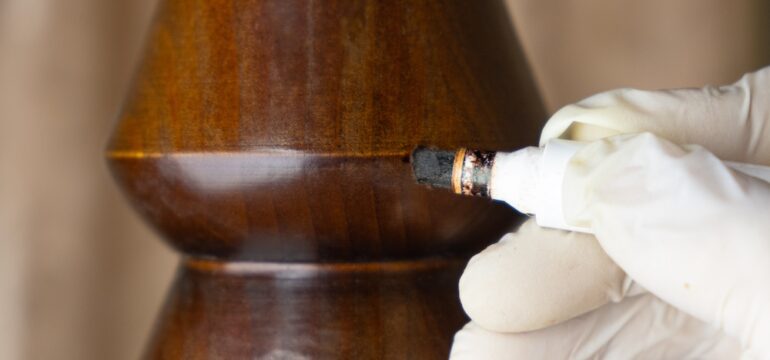 Repairing a flaw in a piece of scratched wooden furniture table leg with a special marker. A close-up photo of restoration of furniture and wooden surfaces.