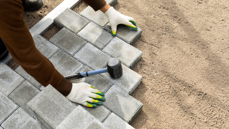Hands of a worker installing a paver patio with a rubber hammer.