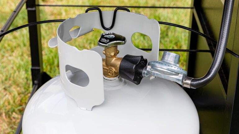 Propane tank with hose and regulator for BBQ grill. Grilling safety, propane tanks equipment inspection and storage.