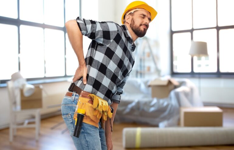 Male worker or builder in helmet having back ache over after the contractor gets hurt on homeowners property.
