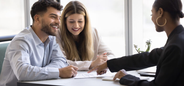 A happy couple engages in conversation with an attorney versus title officer. After reviewing the agreement details, they are ready to sign the contract.