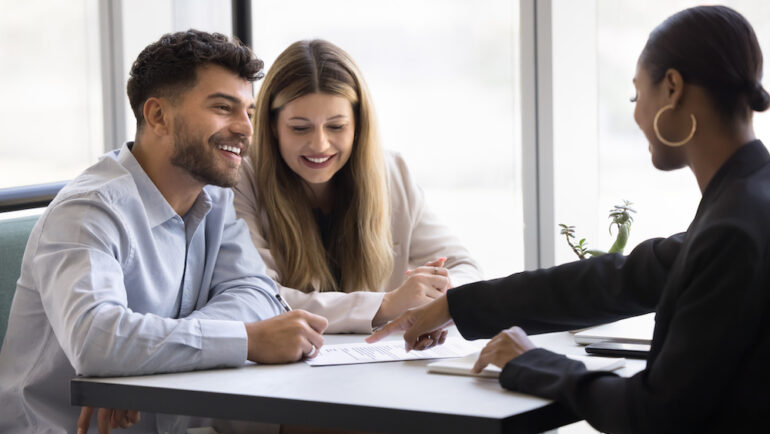 A happy couple engages in conversation with an attorney versus title officer. After reviewing the agreement details, they are ready to sign the contract.