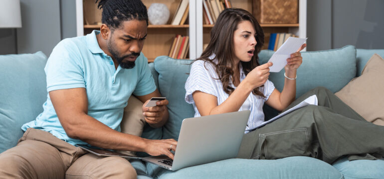 Homeowners’ insurance cost issues. A young couple struggles with utility bills, high insurance costs, and home expenses, as well as financial problems, while paying bills online with a credit card. The concept of cost of living.