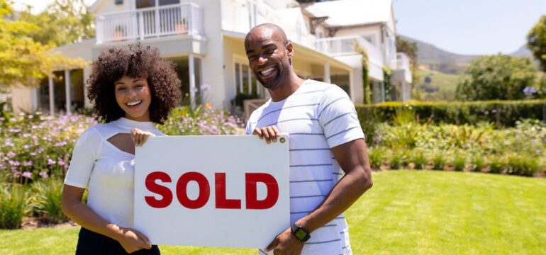 Happy home sellers holding a SOLD sign that use seller concessions to close the purchase of their home.