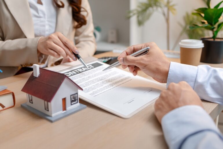 A real estate agent and a client are discussing a home price reduction during a property purchase meeting, showing agreement details and financial negotiation about home ownership.