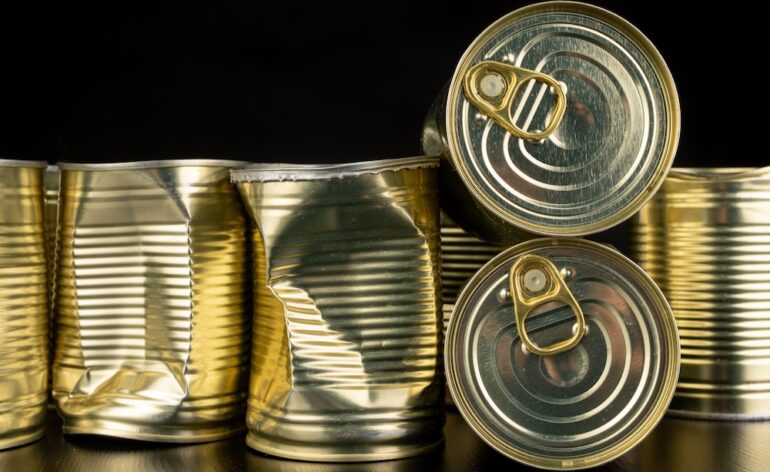 Dented canned food with vegetables on a wooden table.